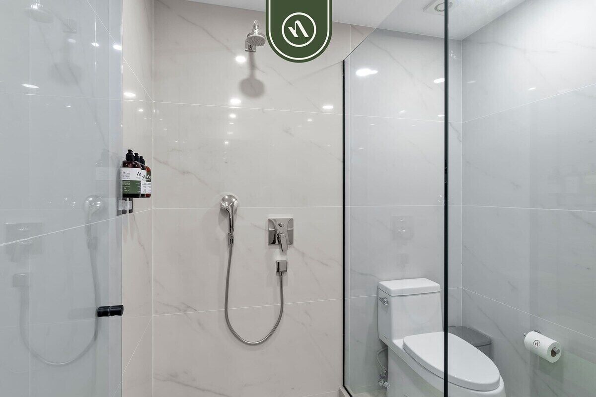 A modern bathroom with a glass shower enclosure, a toilet, and a visible toilet paper dispenser.