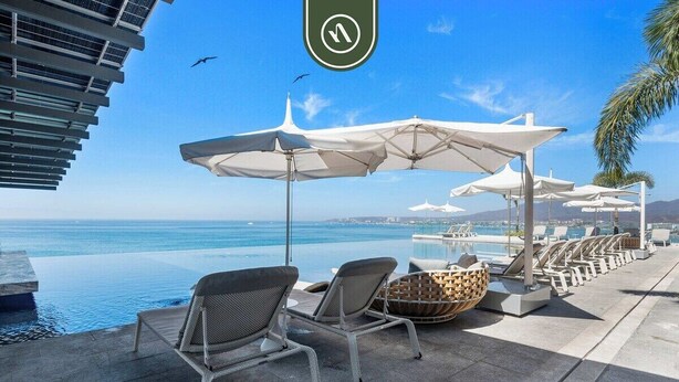 Un espace aménagé au bord de la piscine, avec des chaises longues et des parasols, donnant sur une étendue d’eau.