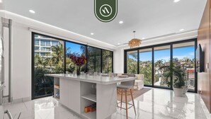 Une cuisine moderne dotée d’un îlot central, de grandes fenêtres et d’une vue sur les palmiers.