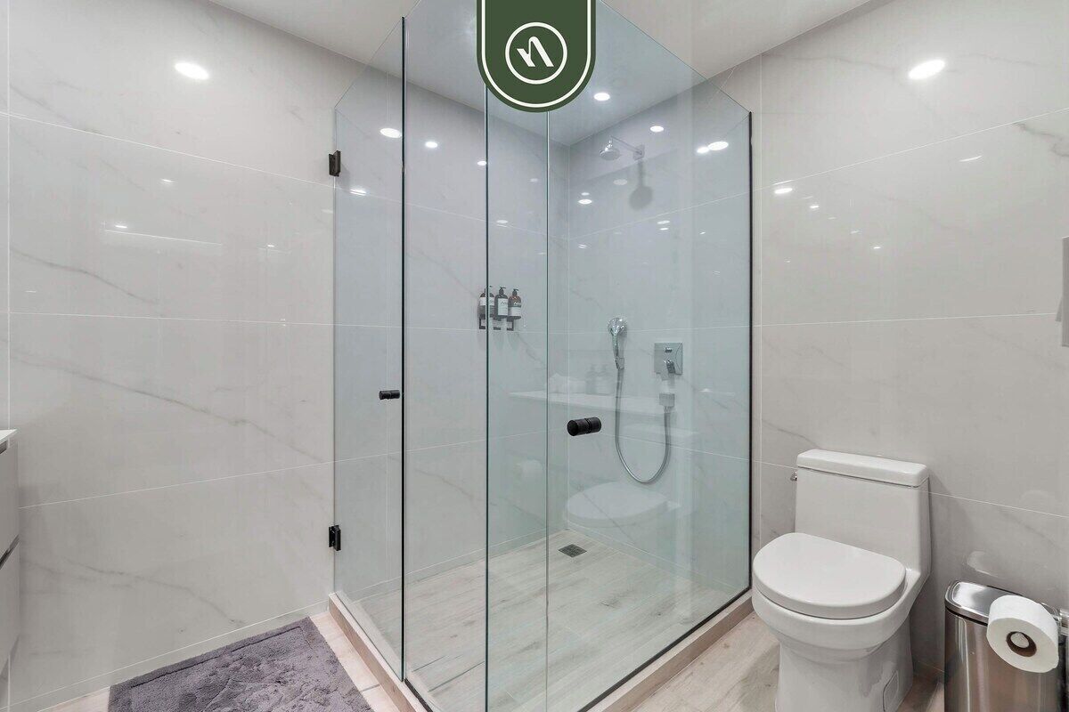 Un bagno moderno con cabina doccia in vetro, un water e un cestino.