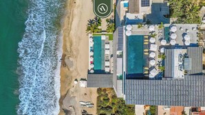 Vue aérienne d’un hôtel situé sur la côte, avec une plage, plusieurs piscines et des espaces de détente en plein air.