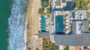 Vista aérea de un hotel costero con playa, múltiples piscinas y zonas de estar al aire libre.