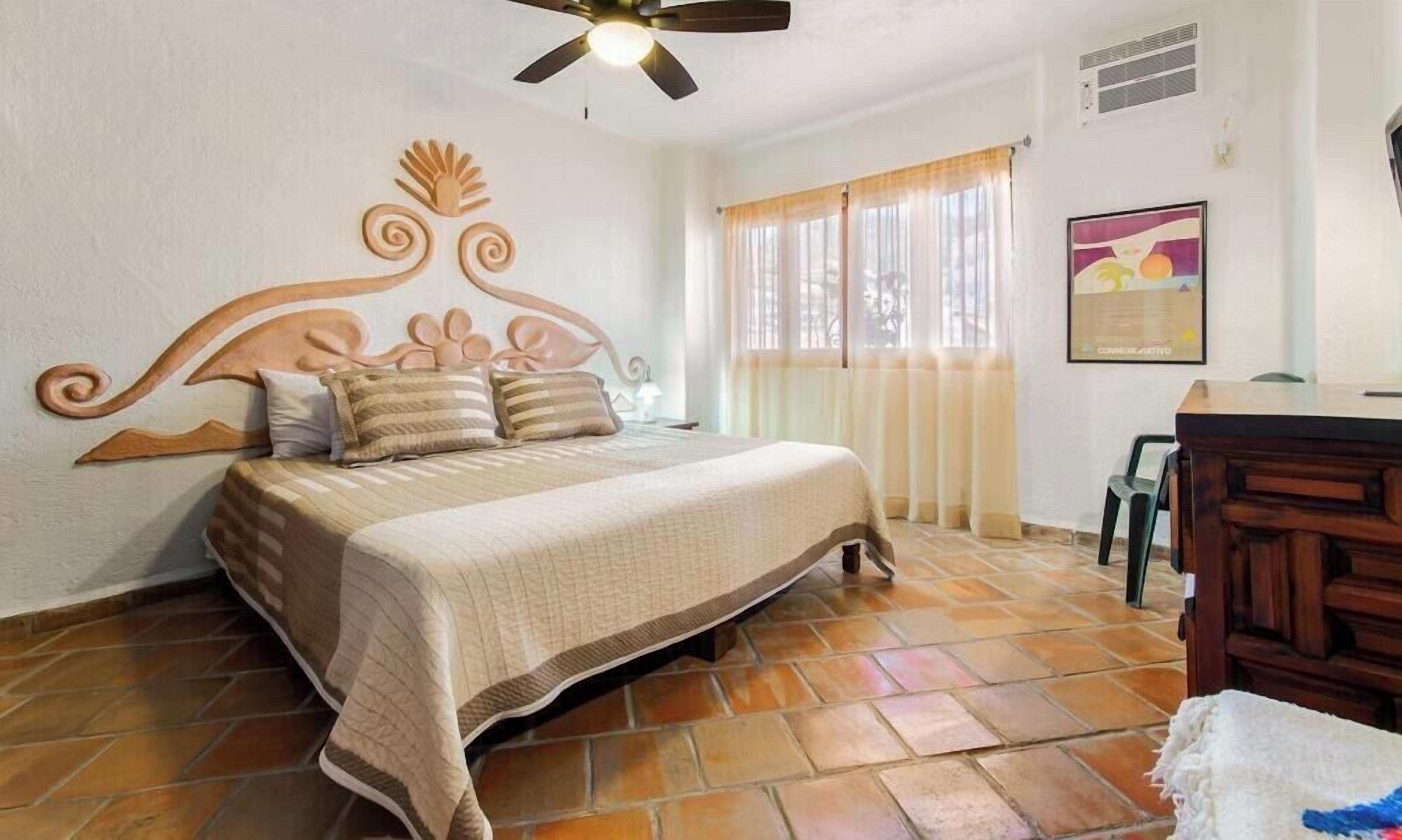 Une chambre à coucher avec un lit, un ventilateur de plafond, une fenêtre avec des rideaux, un bureau et une chaise.
