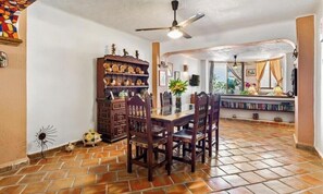 A dining area with a wooden table and chairs, a ceiling fan, and a bookshelf with decorative items.