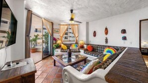 A living room with a sofa, a coffee table, a TV, and a ceiling fan. - Ocean View 2Br Condo-balcony-beach-pool - 304 (Puerto Vallarta)