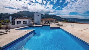 A rooftop swimming pool with a view of mountains, a covered seating area, and a white building. - Ocean View 2Br Condo-balcony-beach-pool - 304 (Puerto Vallarta)
