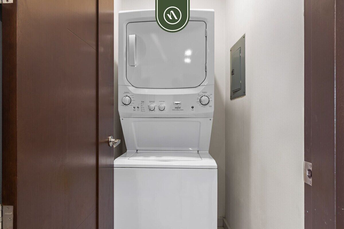 A white washing machine in a bathroom with a door and a wall-mounted electrical outlet.