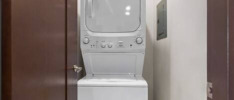 A white washing machine in a bathroom with a door and a wall-mounted electrical outlet.
