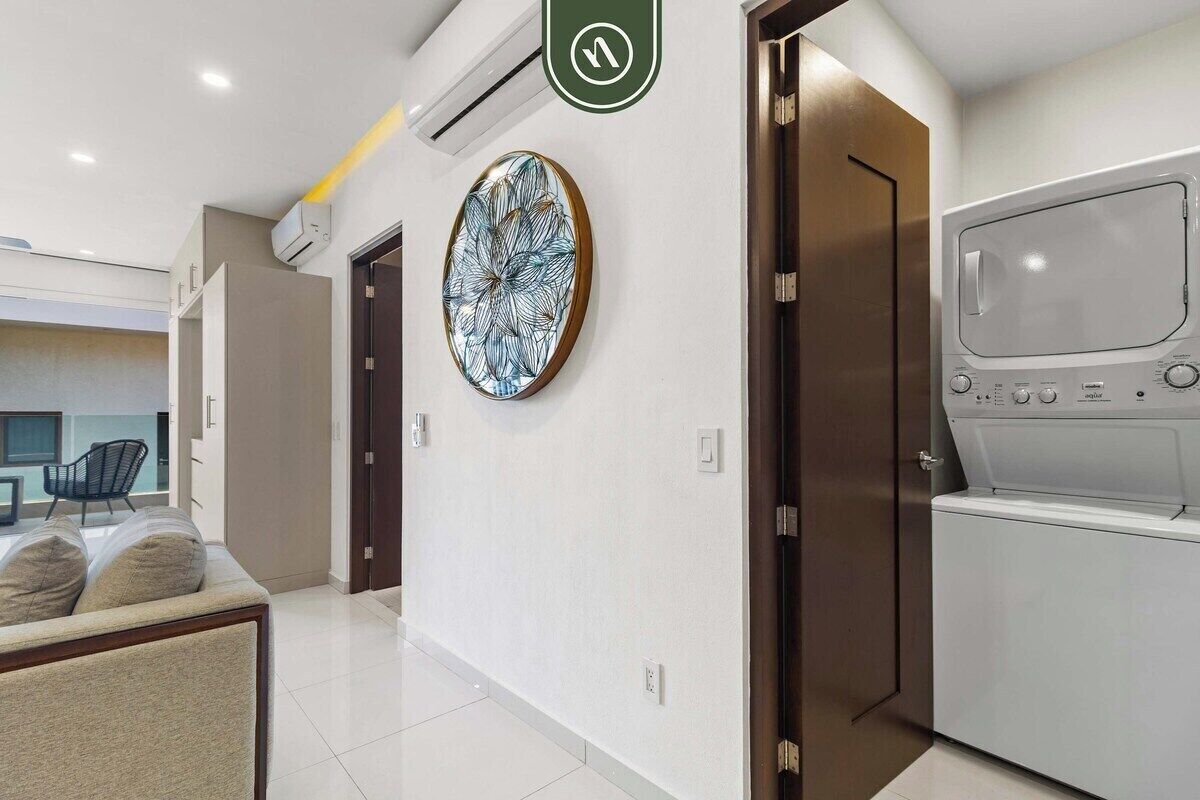 Una habitación de hotel moderna con un ventanal grande, aire acondicionado de pared, un adorno en la pared y lavadora y secadora integradas.
