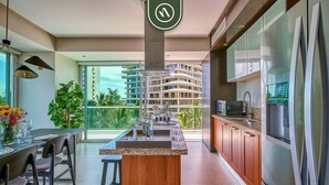 A modern kitchen with a central island, stainless steel appliances, and a view of a high-rise building. - Luxury Oceanfront 2BR Condo With Private Balcony (Puerto Vallarta)