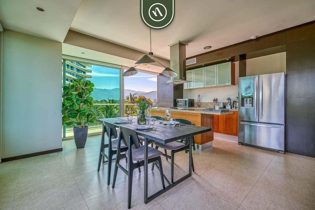 A modern kitchen with a dining area, large windows, and a view of the outdoors.