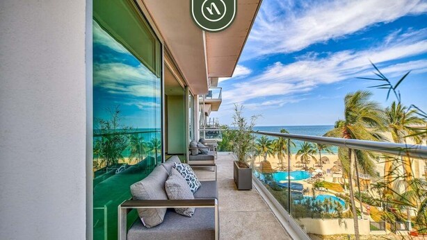 A balcony with a view of a beach and pool, furnished with a sofa and cushions. - Luxury Oceanfront 2BR Condo With Private Balcony (Puerto Vallarta)