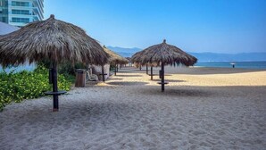 A beach with thatched umbrellas and a clear view of the sea. - Luxury Oceanfront 2BR Condo With Private Balcony (Puerto Vallarta)