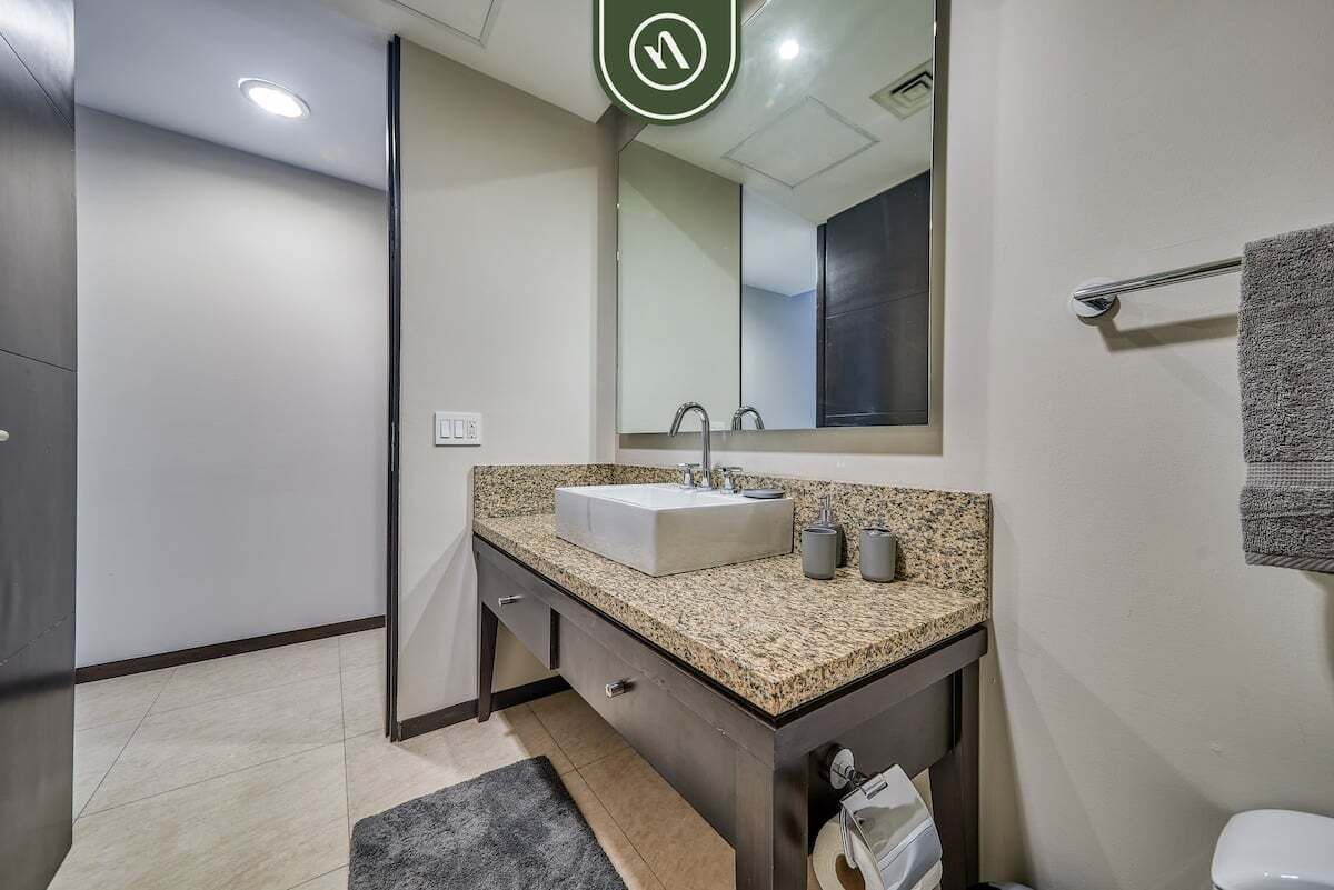 Een moderne badkamer met een wastafel met granieten blad, een grote spiegel en een handdoekrek.