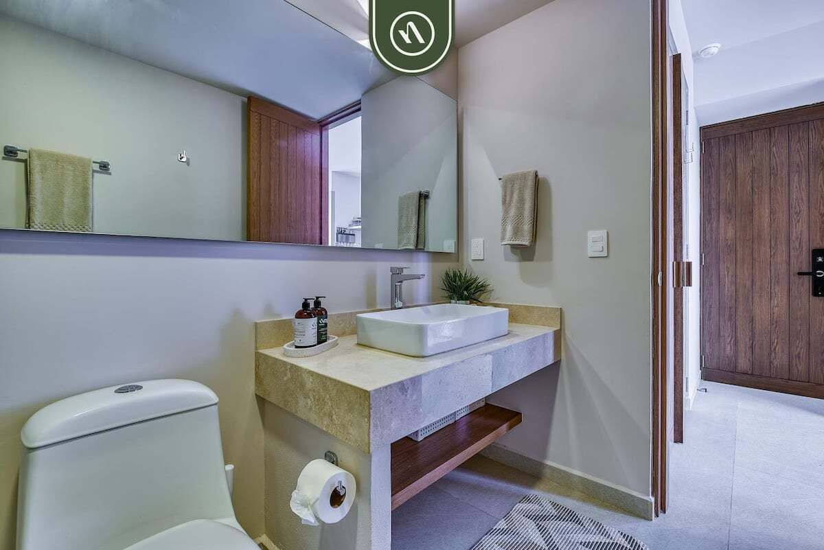 A modern bathroom with a white toilet, a beige sink, and a large mirror.