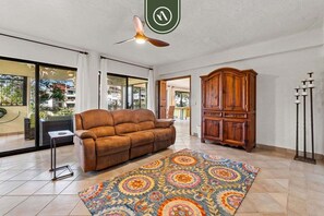 Un salon avec un canapé marron, un tapis à motifs, un meuble en bois et un ventilateur de plafond.