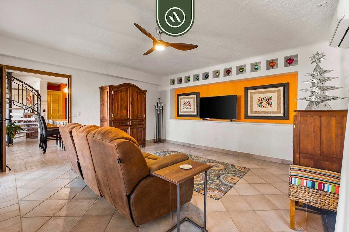 Un salon avec un canapé, un téléviseur, un ventilateur de plafond et un escalier.