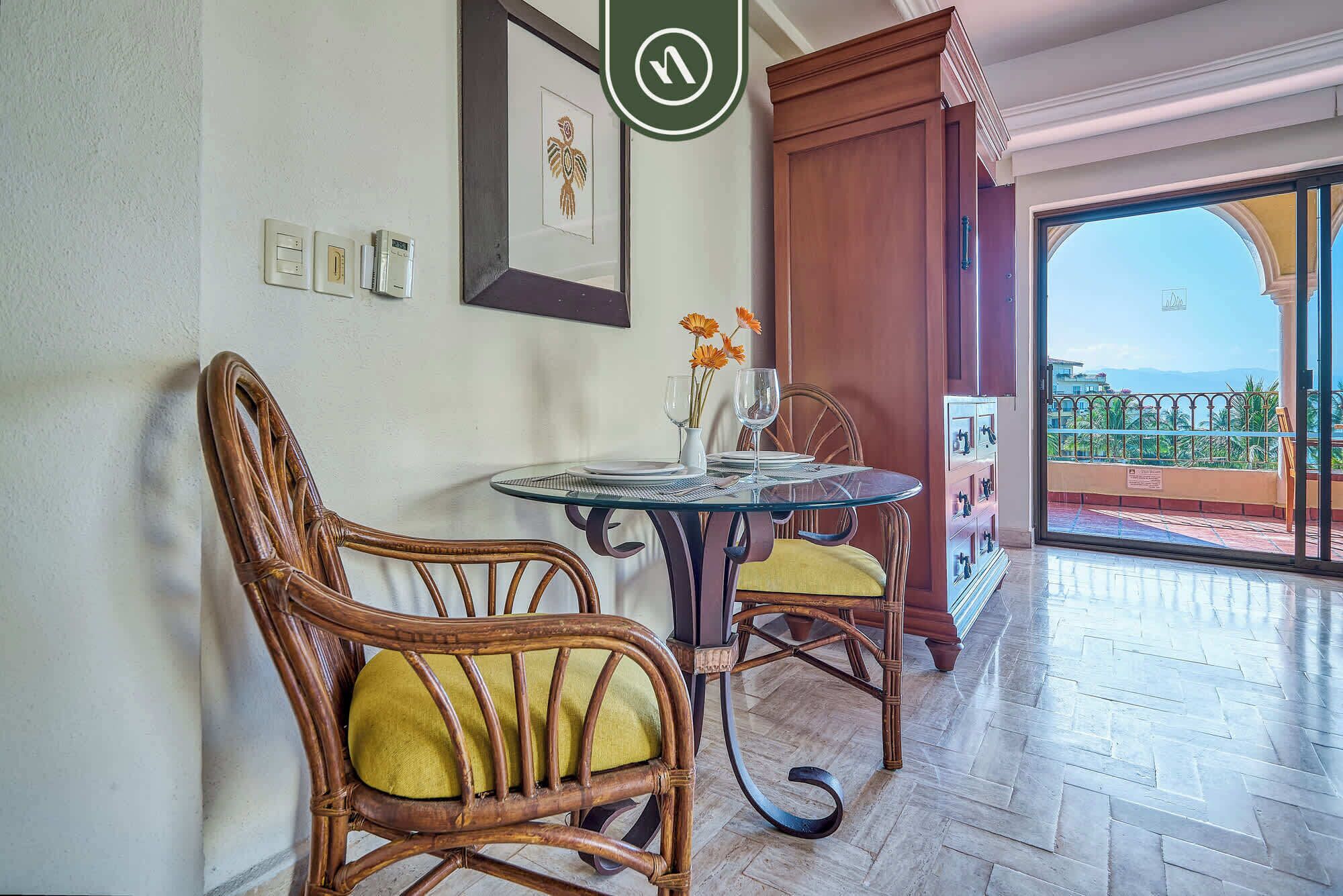 Un comedor con sillas de mimbre, una mesa de vidrio y vistas a un balcón con barandilla.