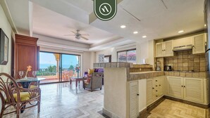A spacious living area with a balcony, a dining area, and a kitchen with wooden cabinets. - Beachfront 2 BR Condo - Beach - Pools - Tennis (Puerto Vallarta)