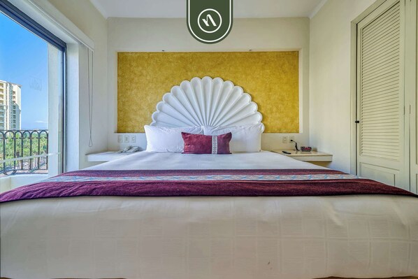 A hotel room with a large bed, a gold accent wall, a balcony with a view, and a door with a handle. - Beachfront 2 BR Condo - Beach - Pools - Tennis (Puerto Vallarta)