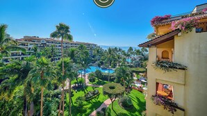 A resort with a pool, palm trees, and a view of a mountain range. - Beachfront 2 BR Condo - Beach - Pools - Tennis (Puerto Vallarta)