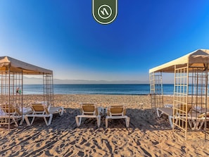 A beach with sun loungers and umbrellas, a clear sky, and a calm sea.