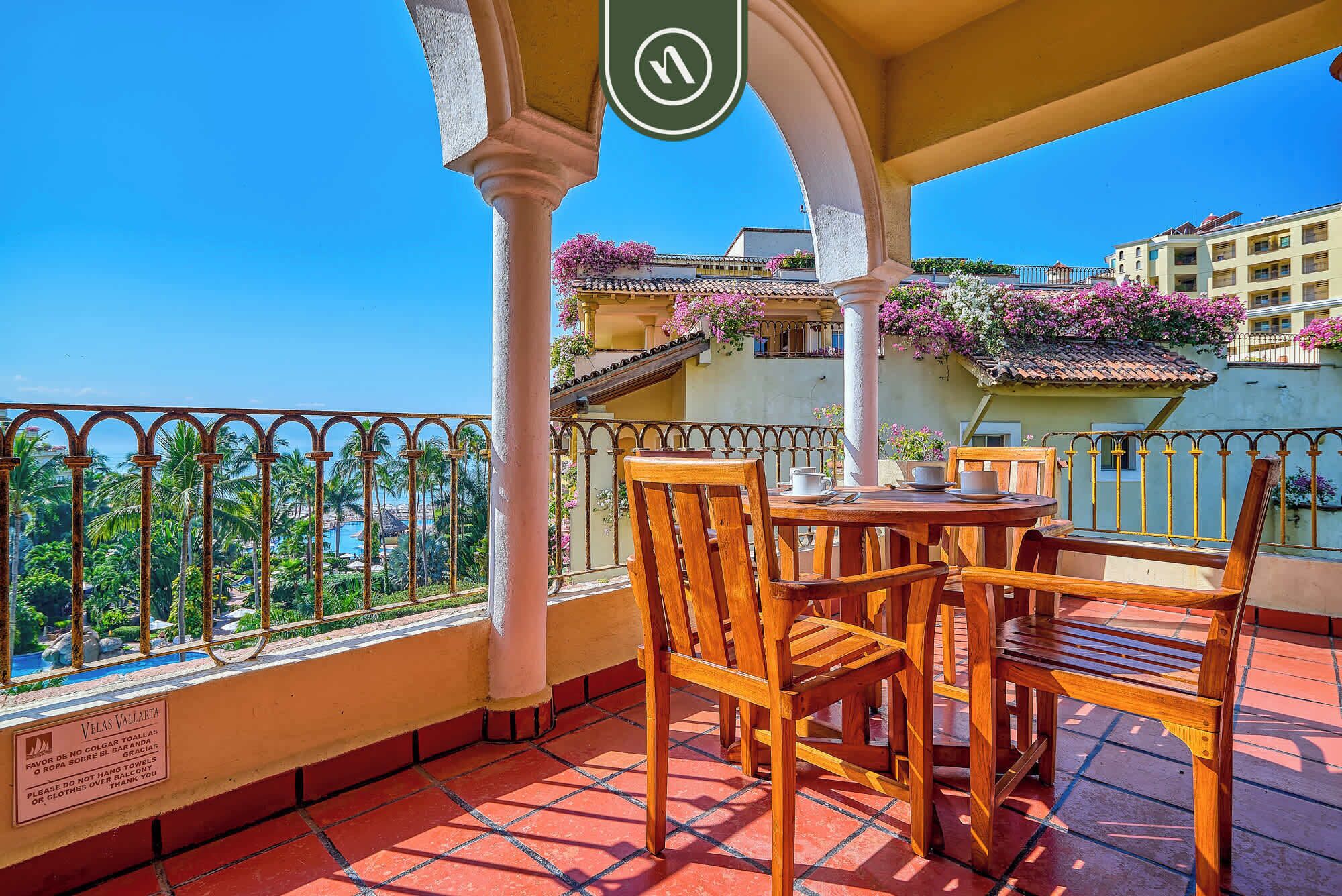 Balcón con mesa y sillas, con vista a una piscina y vegetación.