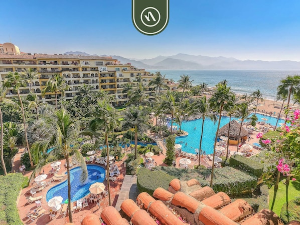 A resort with multiple swimming pools, palm trees, and a view of the sea.
