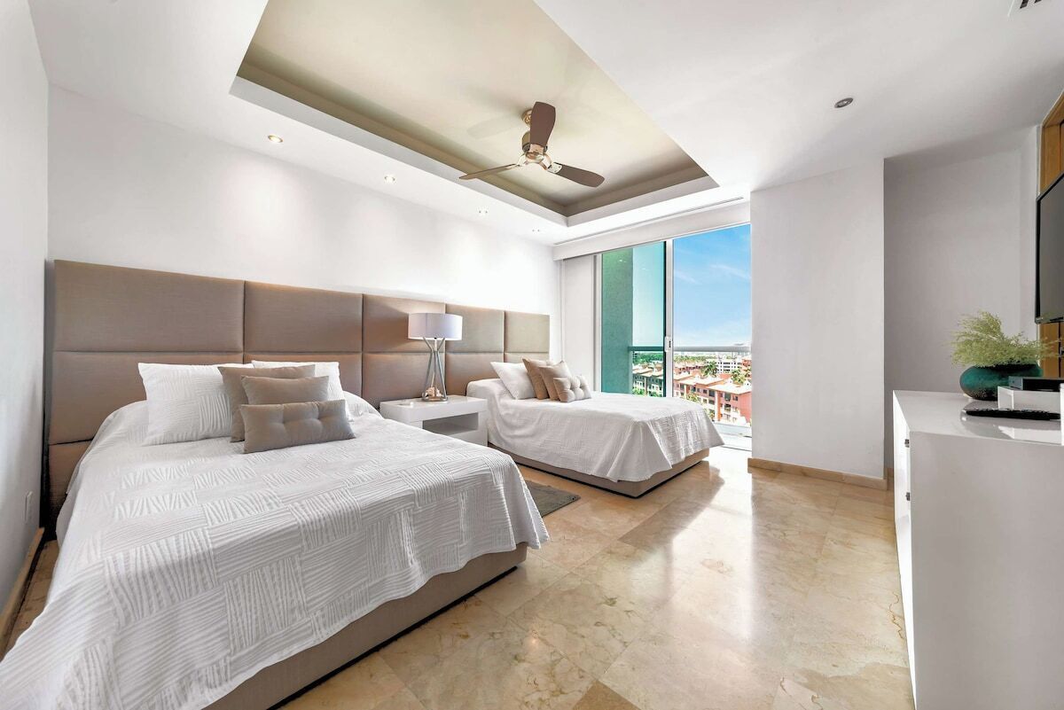 Ein modernes Hotelzimmer mit zwei Betten, einem Deckenventilator, einem großen Fenster mit Blick und einem Flachbildfernseher.