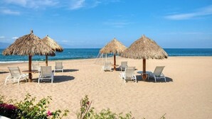 A beach with thatched umbrellas and white lounge chairs. - Luxury Oceanfront 4BR Condo - Pool - Ocean View (Puerto Vallarta)