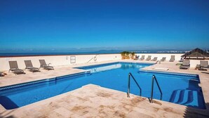 Une piscine sur le toit, avec une eau d’un bleu cristallin, entourée de chaises longues et offrant une vue sur l’océan.