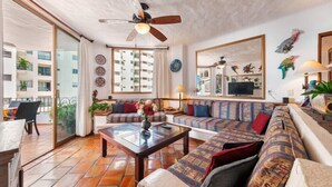 Un salon avec un canapé, une table basse et un ventilateur de plafond. Il y a un balcon avec vue sur les immebles.