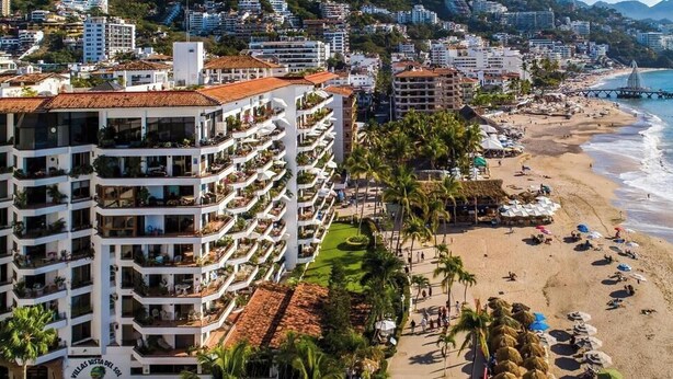 Un hôtel situé sur la côte, doté de nombreux balcons, d’une plage et offrant une vue sur la mer.