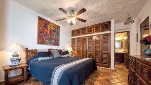 Une chambre à coucher avec un lit, un ventilateur de plafond, une armoire en bois et un plancher carrelé.