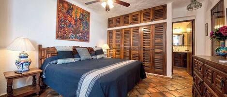 Un dormitorio con cama, ventilador de techo, armario de madera y suelo de baldosas.