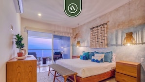 Ein Schlafzimmer mit Bett, Nachttischen, einer Bank, einem Schreibtisch und Blick ins Freie.