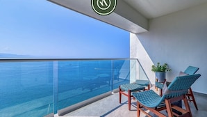 Ein Balkon mit Glasgeländer, zwei Holz-Loungesessel und einem Topfpflanzen.