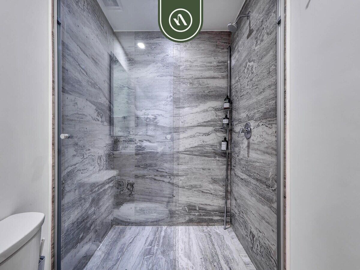 A modern bathroom with a glass shower enclosure, marble walls, and a toilet.