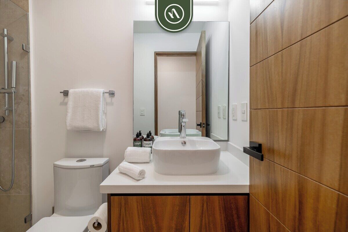 A modern bathroom with a white sink, a toilet, a shower, and a wooden vanity.