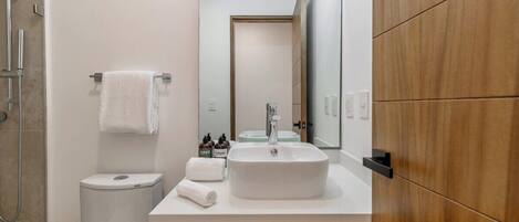 A modern bathroom with a white sink, a toilet, a shower, and a wooden vanity.