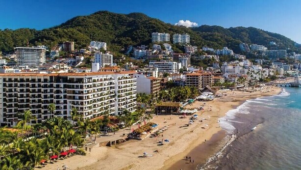 A coastal cityscape with a beach, buildings, and a mountain backdrop.