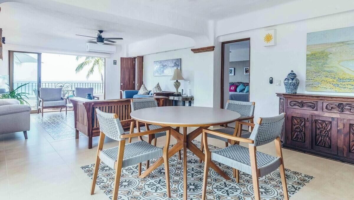 A spacious living room with a round wooden table surrounded by wicker chairs, a sofa, and a cabinet with intricate carvings.