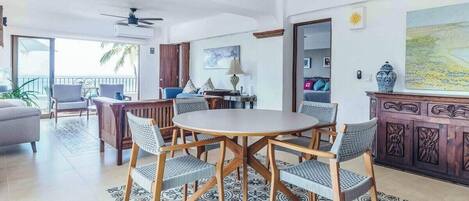 A spacious living room with a round wooden table surrounded by wicker chairs, a sofa, and a cabinet with intricate carvings.