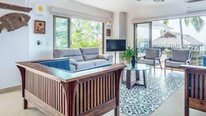 A spacious living room with a large wooden coffee table, grey sofas, and a TV.