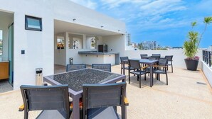 Une terrasse sur le toit équipée d’une table à manger, de chaises, d’un petit coin cuisine et d’une plante en pot.