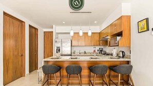 Une cuisine moderne avec des meubles en bois, un îlot central doté de tabourets de bar et un luminaire suspendu.