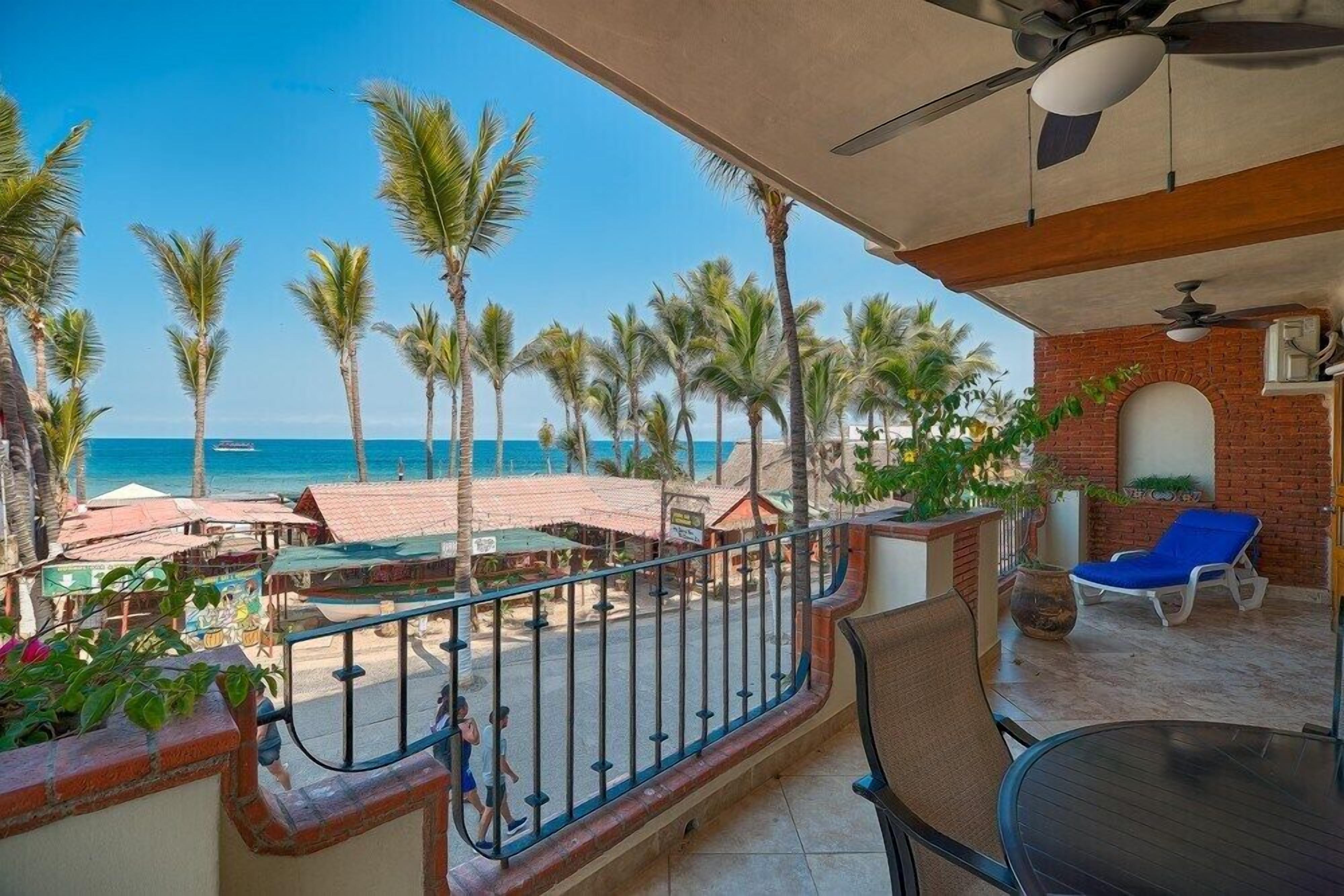 Un balcon avec vue sur la plage, les palmiers, et un espace repas comprenant des chaises et une table.