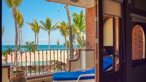 Un balcón con vista a la playa y palmeras, una planta en maceta y un sillón azul con cojines.