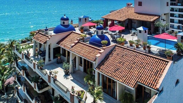Un hotel con varios edificios de cúpulas azules, una piscina y vista al mar.