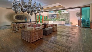 A spacious lobby with wicker furniture, a chandelier, and a view of greenery outside. - 1 BR Condo in Romantic Zone - Amazing Rooftop Pool (Puerto Vallarta)